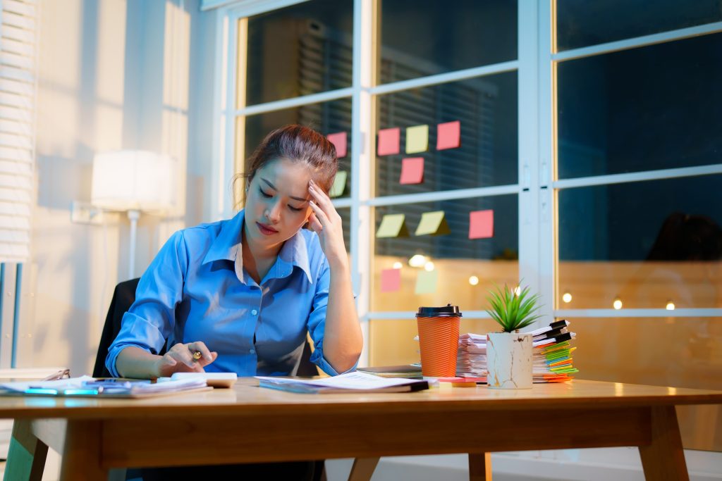Stressed woman sitting at desk at night feeling overwhelmed and mentally exhausted